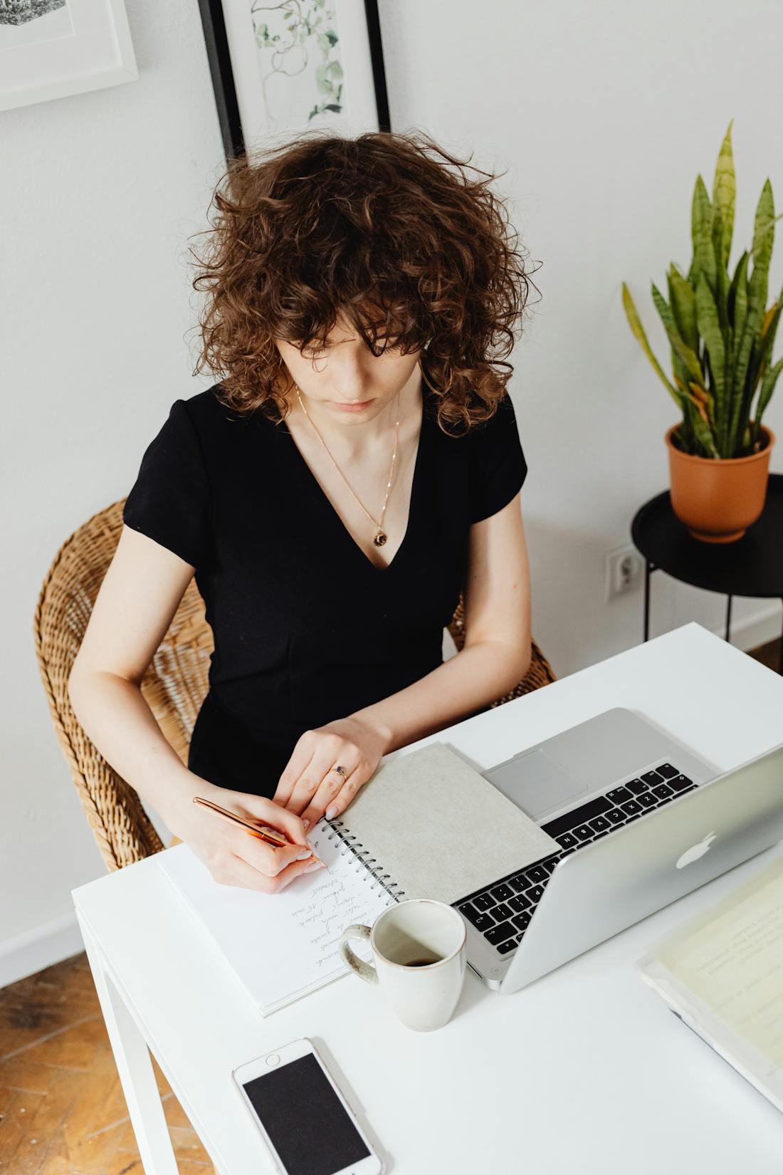 Woman focused writing at her desk after enjoying brain boosting snack combos, with laptop, notebook, mug and phone nearby