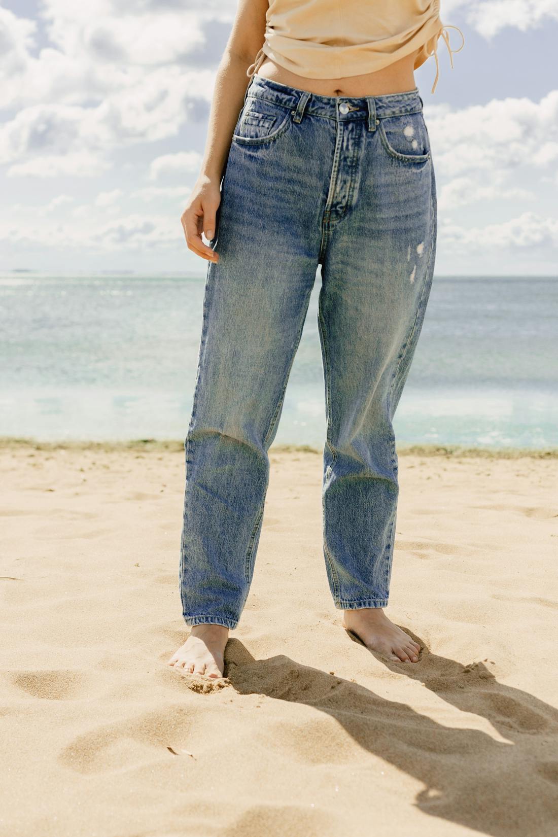 Woman standing barefoot on sandy beach, illustrating the benefits of barefoot walking for foot health, balance, and whole-body energy.