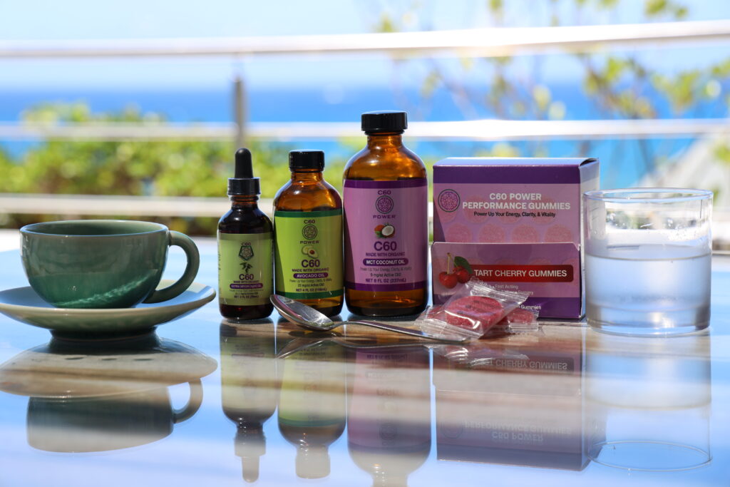 C60 Power MCT Oil, Avocado Oil, Tart Cherry Gummies and olive oil C60 supplements displayed on a table by the sea to illustrate c60 mitochondria support and daily energy routine
