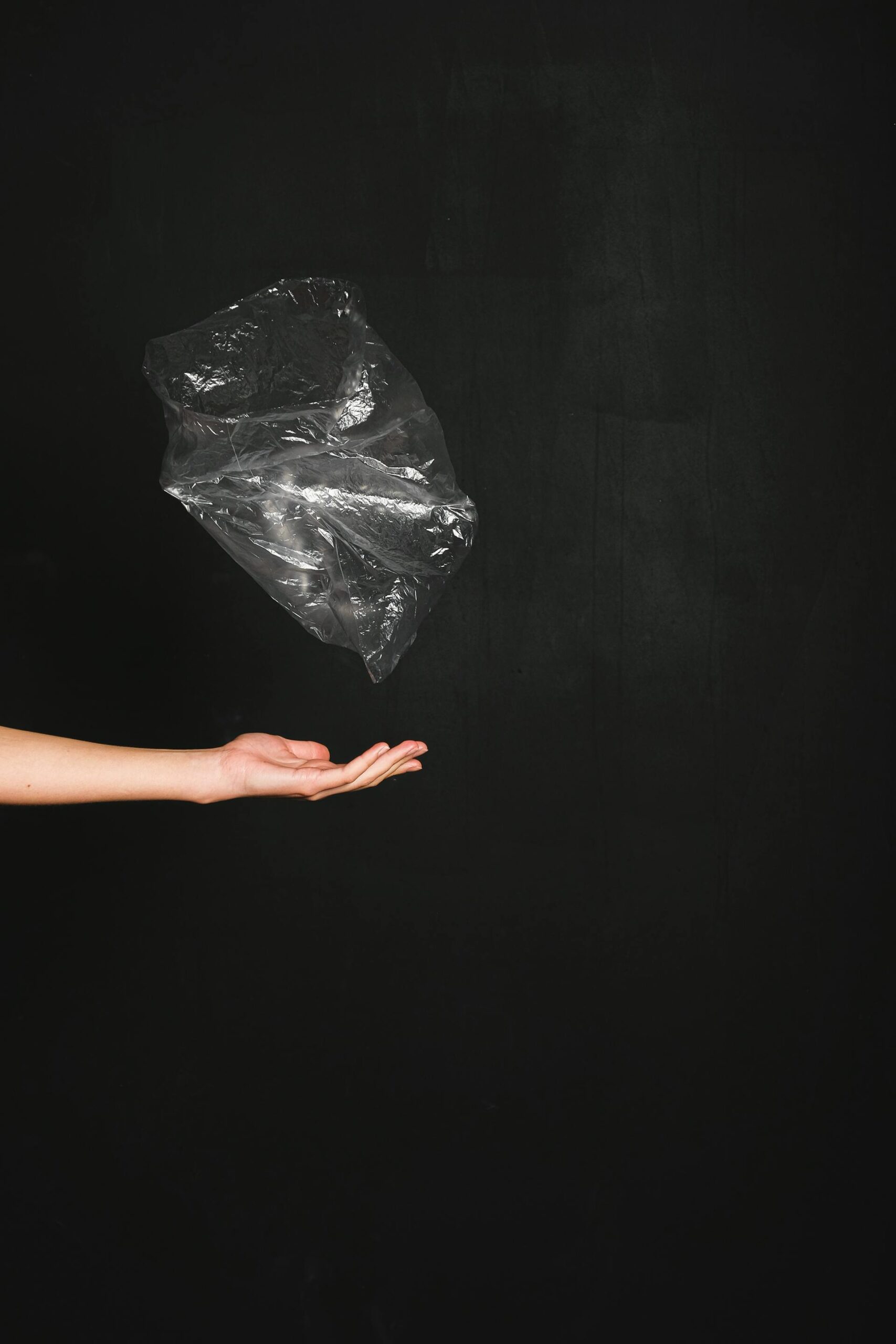 Hand tossing a plastic bag against a black background, symbolizing plastic removal in a microplastic detox protocol
