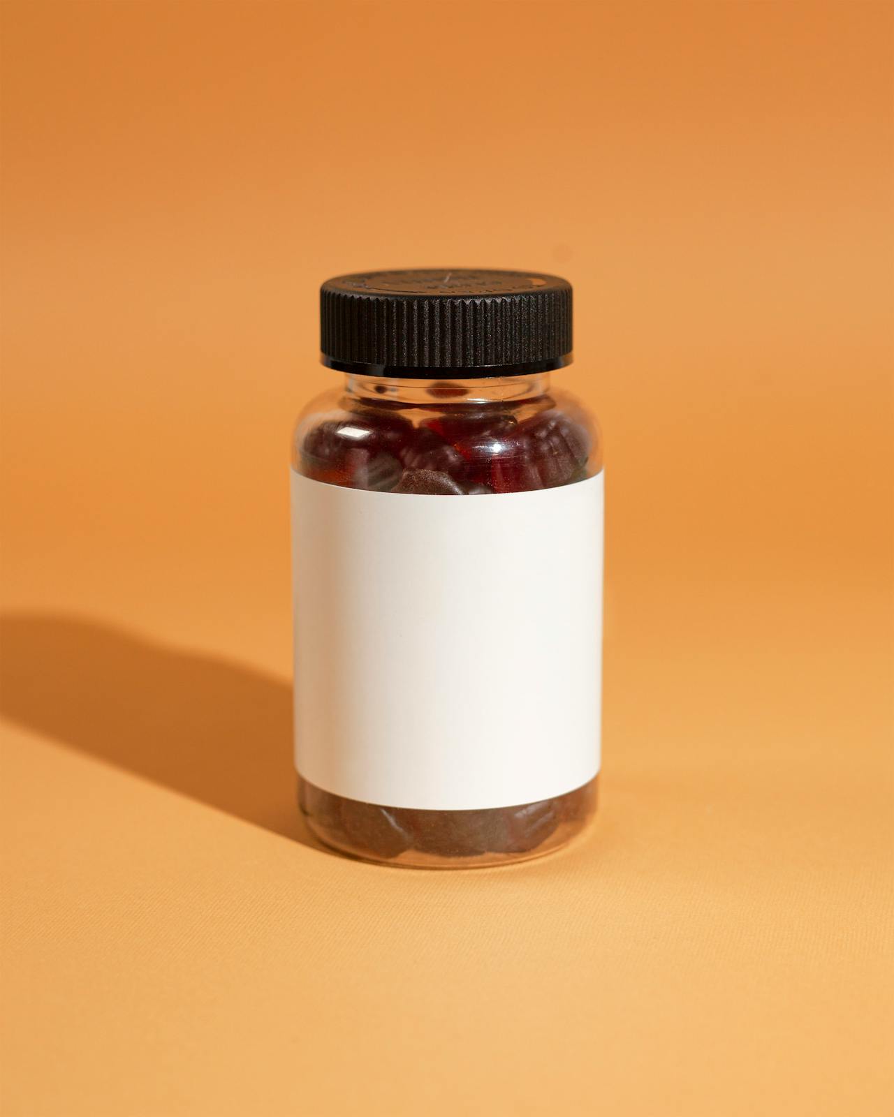 Clear bottle of red gummy supplements with blank label on orange background, illustrating how to read supplement labels for dose, form, and testing.