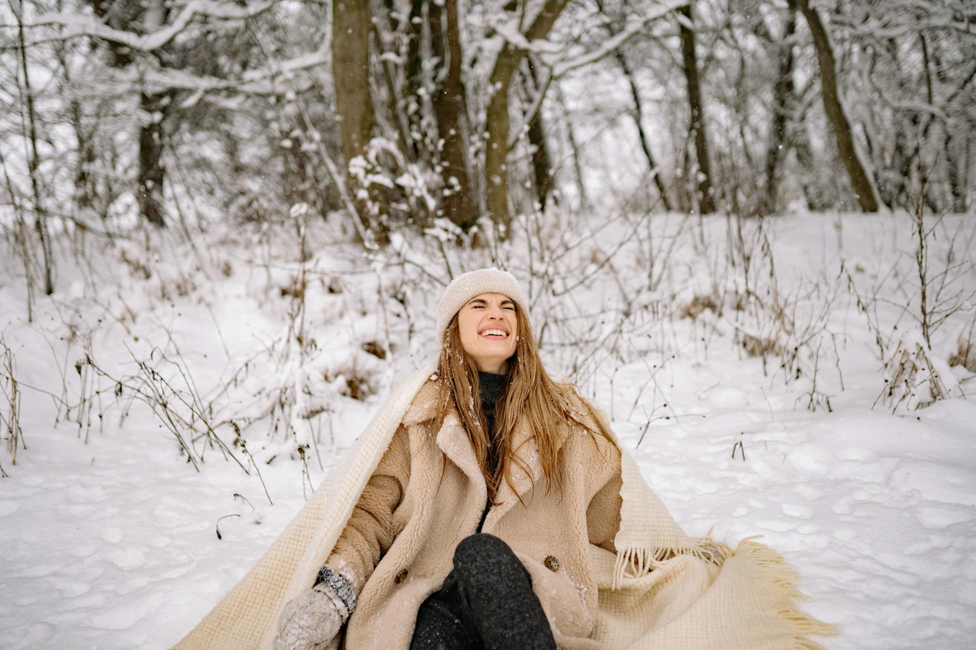 Smiling woman sitting in snowy forest during winter, representing winter mood support supplements and simple lifestyle habits for better energy and mood
