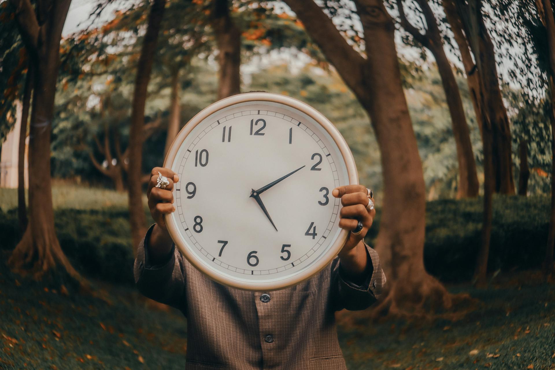 Person holding a large clock outdoors in a forest, representing meal timing and intermittent fasting benefits and risks.