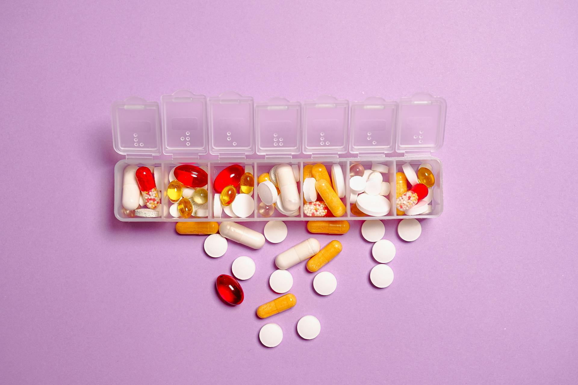 Supplement pyramid featured image showing a weekly pill organizer filled with capsules, tablets, and softgels on a purple background, representing how to prioritize supplements in a daily routine.